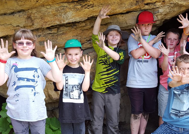 Group of kids smiling with hands raised outside of small cave
